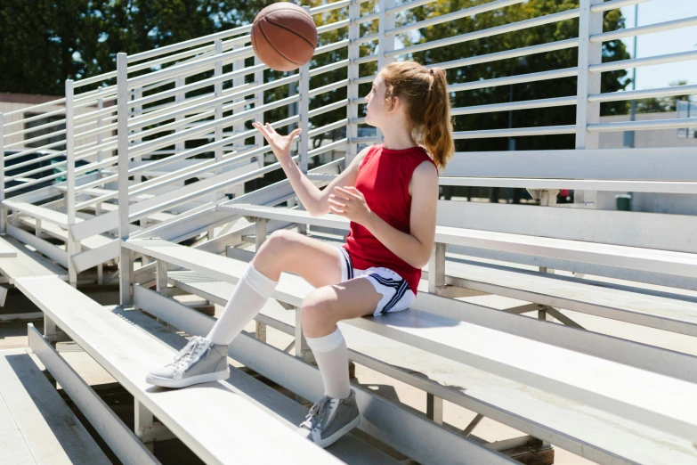 a little girl sitting on a bench with a basketball