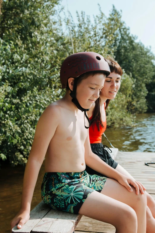 two little s sit on a wooden pier in front of the river