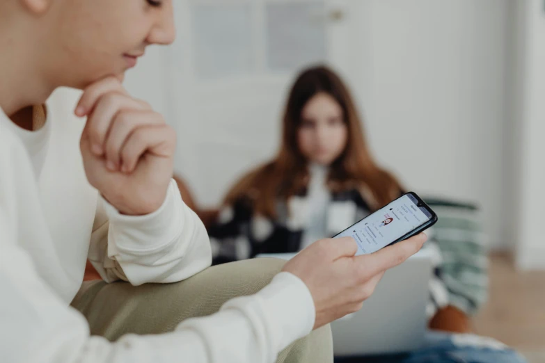 two people sitting on a couch one looking at her phone the other looking down