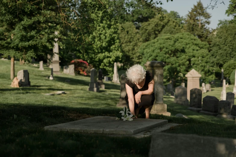 a woman kneeling at the grave next to a memorial