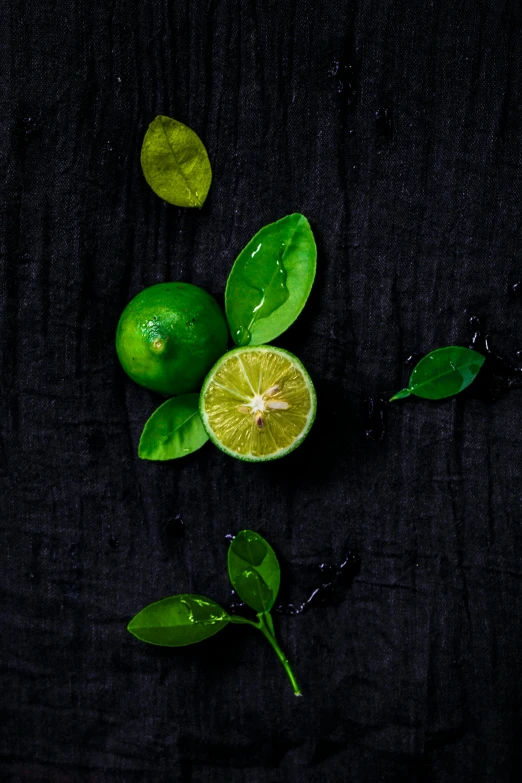 an arrangement of green fruits with leaves, on a black cloth