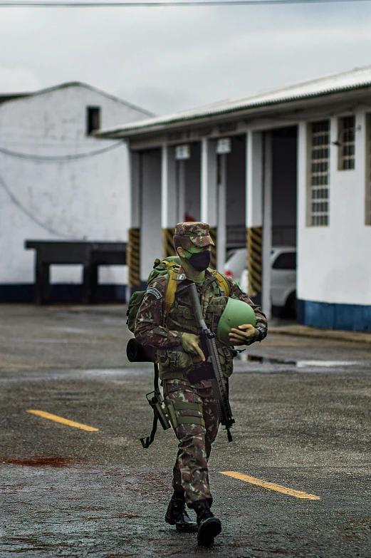 the man in camouflage is walking in front of two white buildings