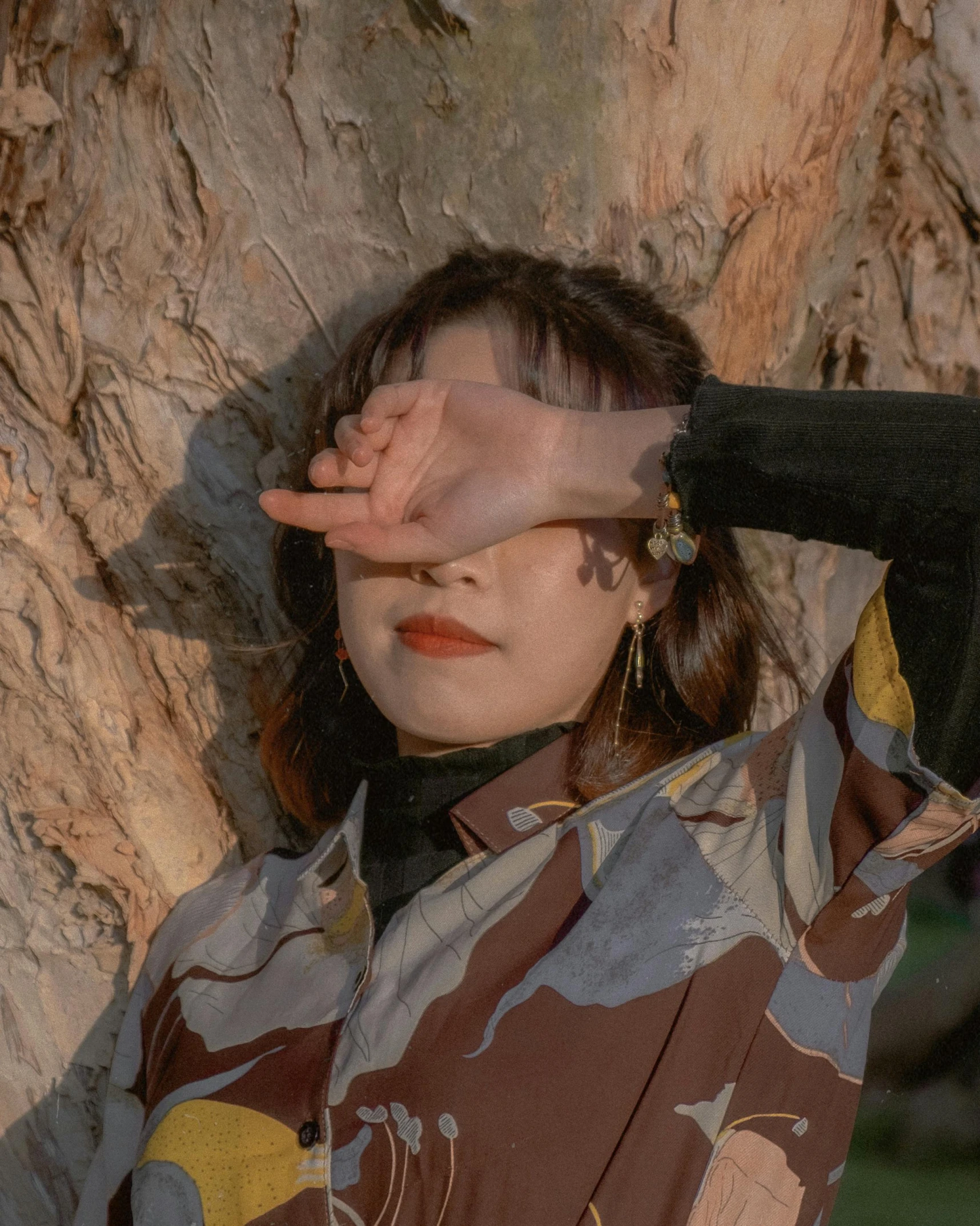 a woman covering her eyes and a tree trunk