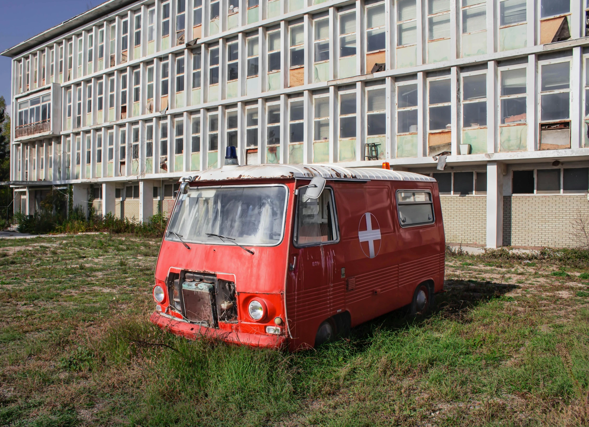 an old red van parked in the grass in front of a building