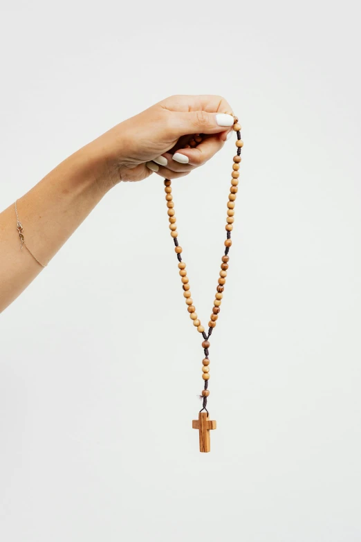 a person holds a rosary with a small cross in its palm