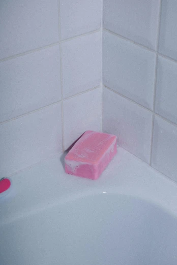 a pink container sits on the edge of a bathtub