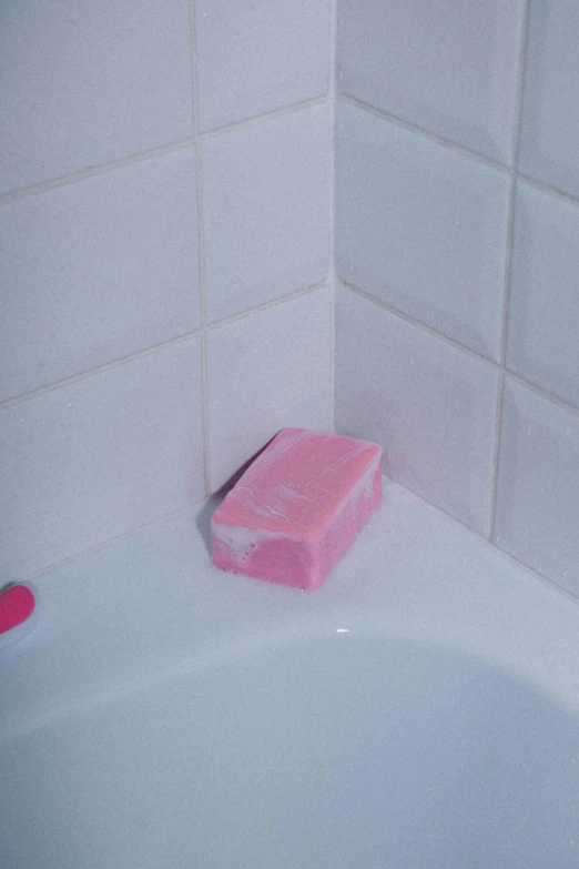 a pink container sits on the edge of a bathtub