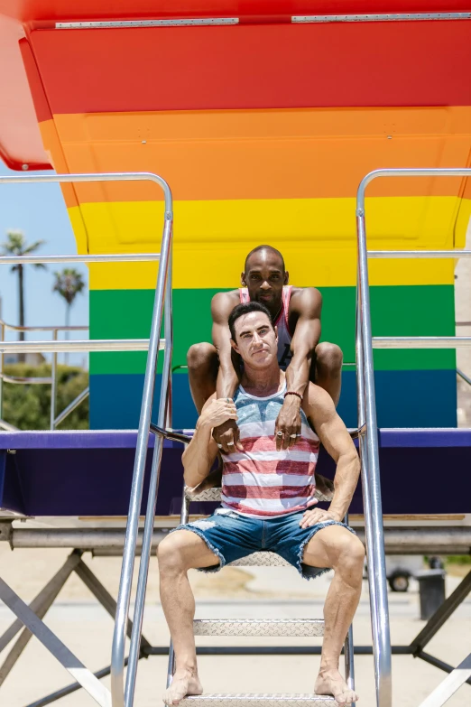 a man and child sitting on a lifeguard chair in front of a rainbow colored background