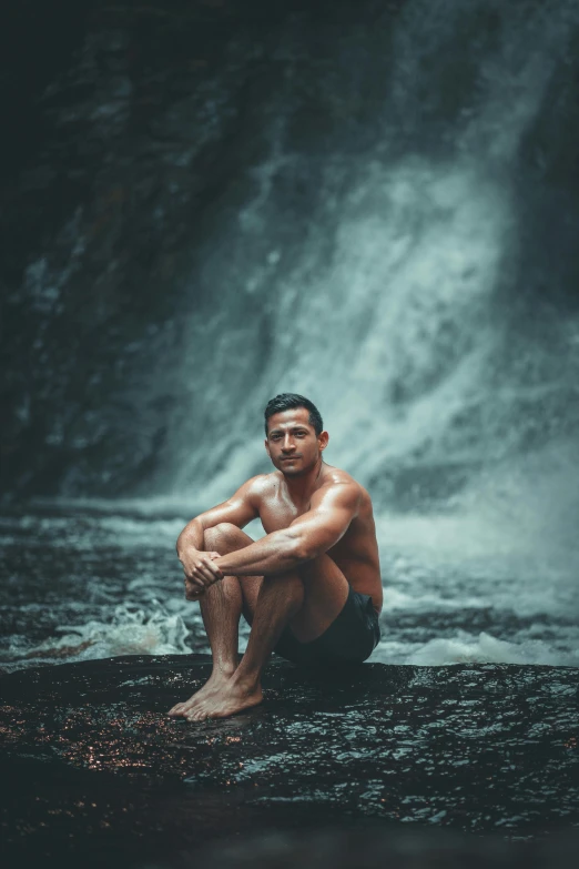 a  man sitting by a waterfall in the rain