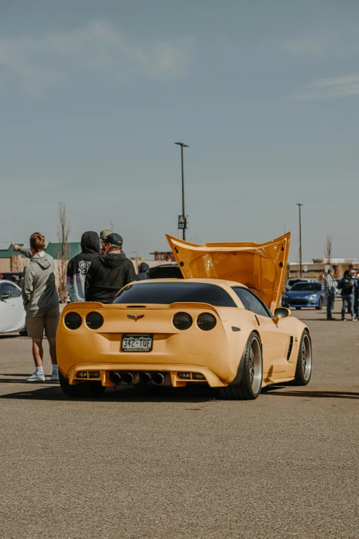 people standing around a yellow car in an open lot