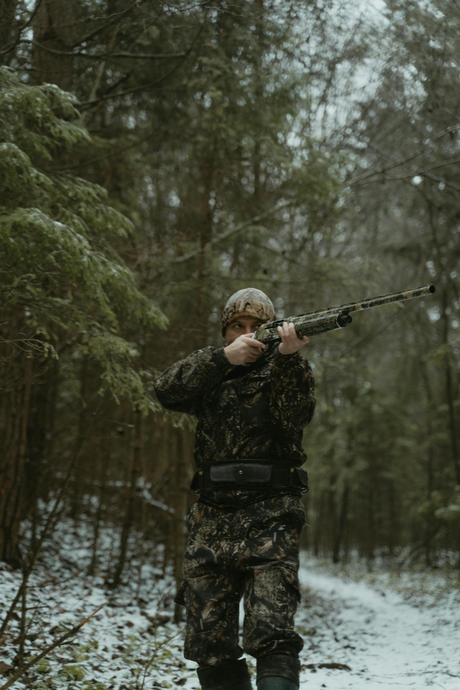 man wearing camouflage aiming a rifle in the snowy woods