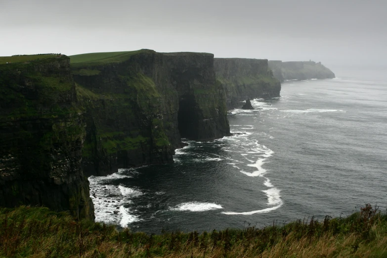 a large ocean cliff sitting on top of a lush green hillside