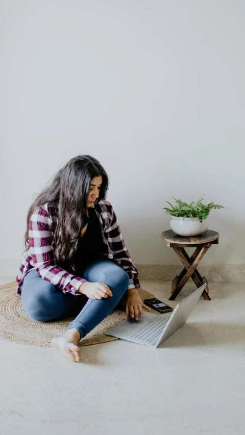 a person with long hair on her knees sits on the floor and uses a laptop computer