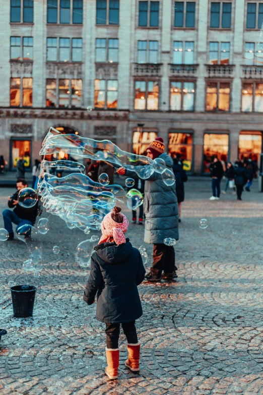 people in winter coats and rubber boots are outside, playing with bubbles