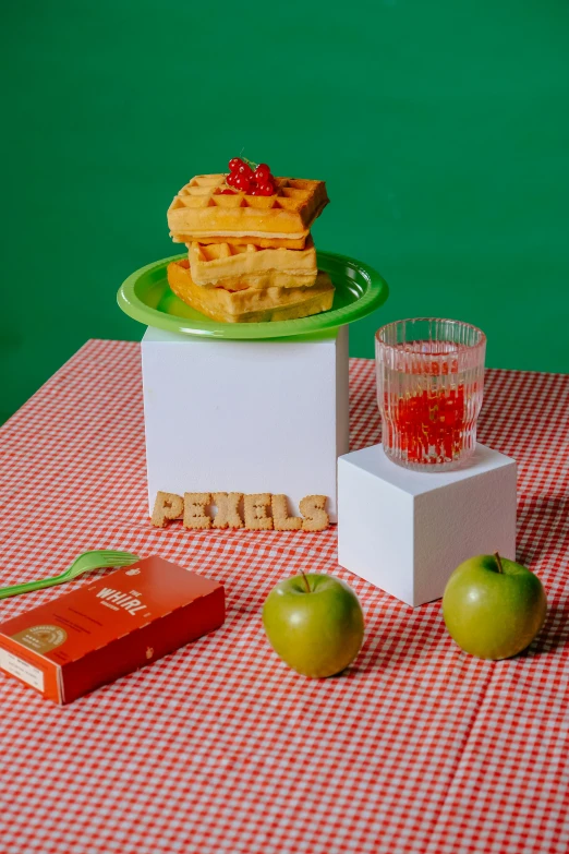 some apples on a red and white table with a glass and some waffles