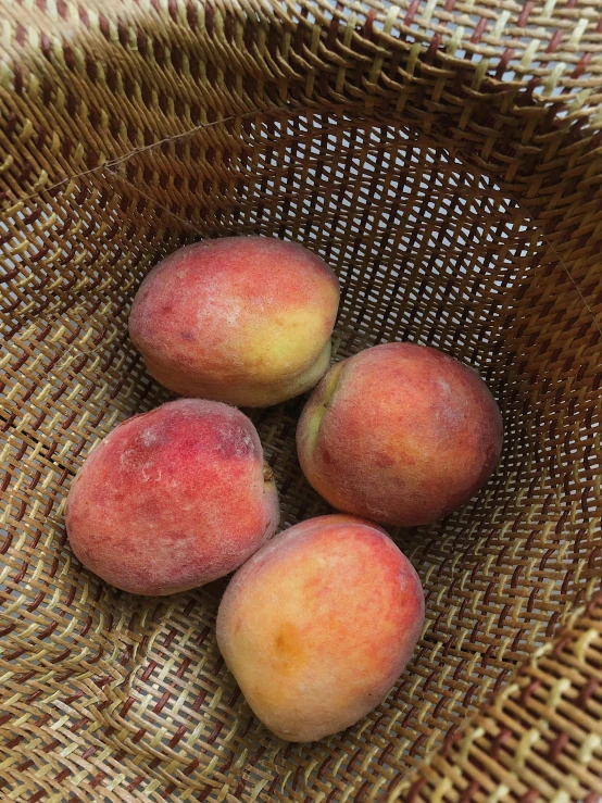 a woven bag filled with four small peaches