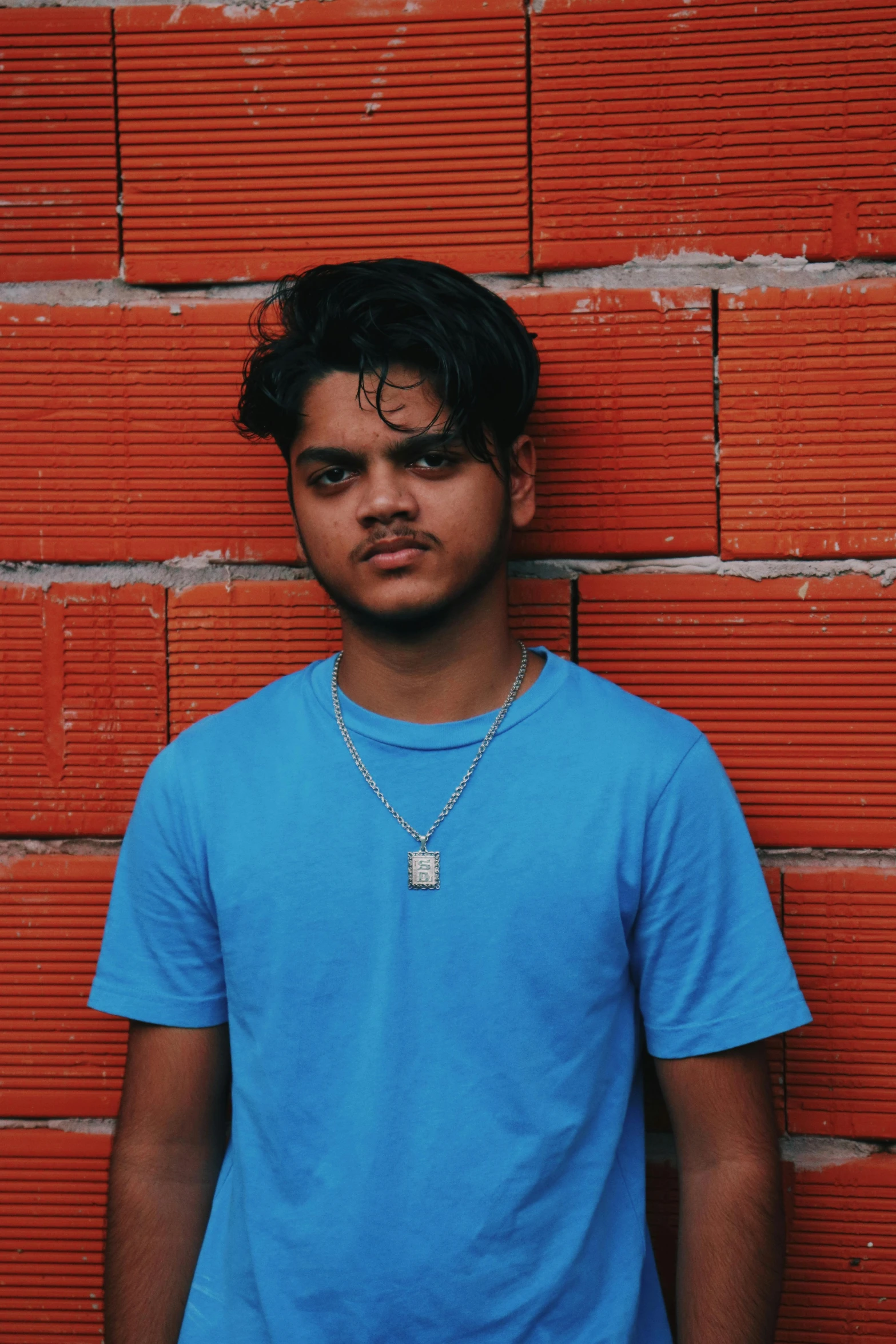 a young man in blue t - shirt leaning against red brick wall