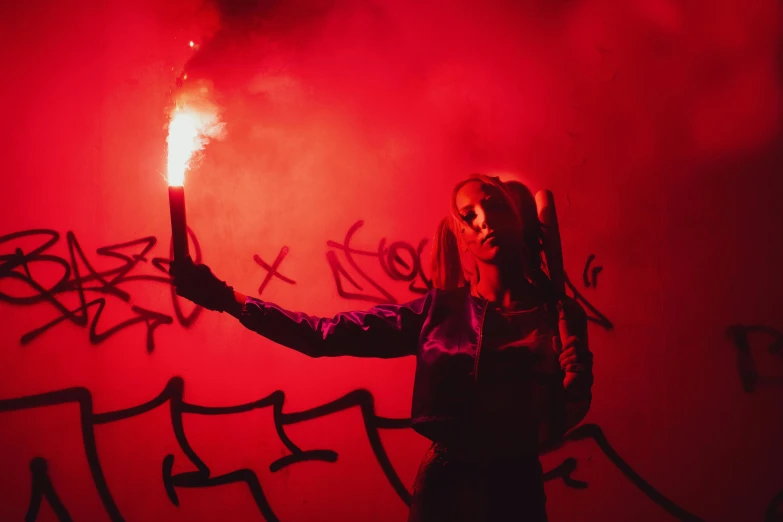 a girl holding a sparkler on fire against graffiti