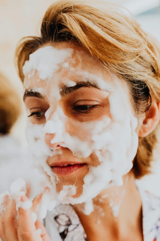 woman holding a foam and smiling while touching her face