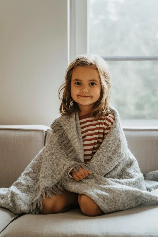 little girl wrapped in blanket sitting on sofa