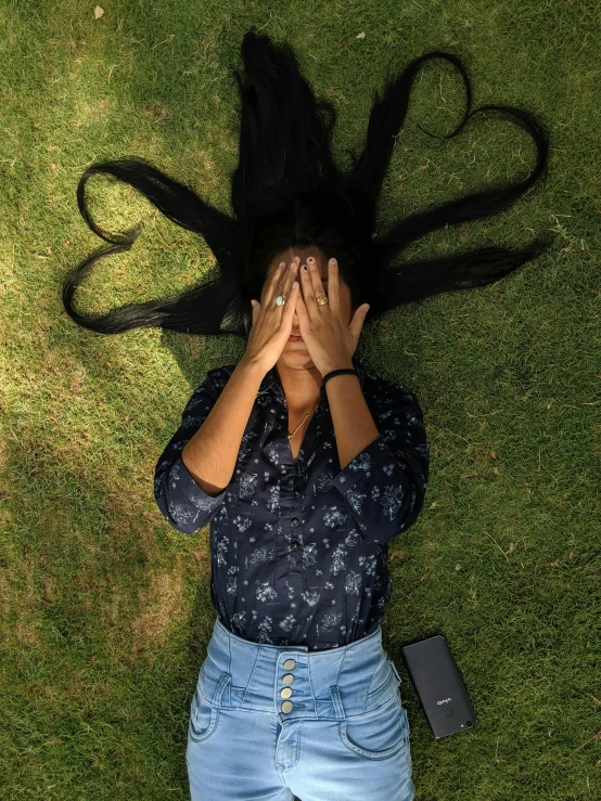 a woman with long black hair covering her eyes lying in the grass