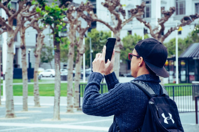 man with black backpack taking a picture on his cellphone