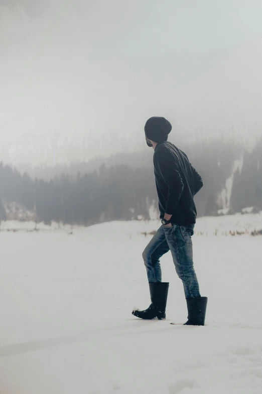 man in a black jacket walking across a snow covered ground