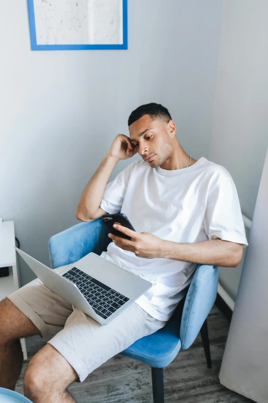 a man sits in an office chair while he uses his phone and laptop