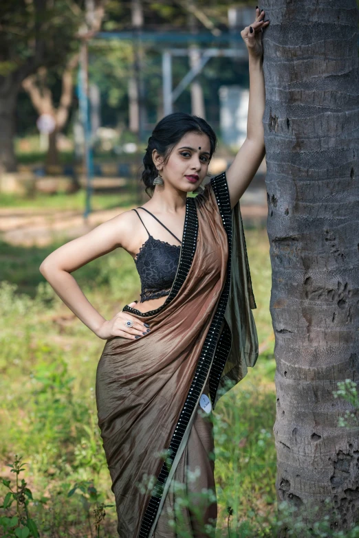 a young woman in indian sari standing near a tree