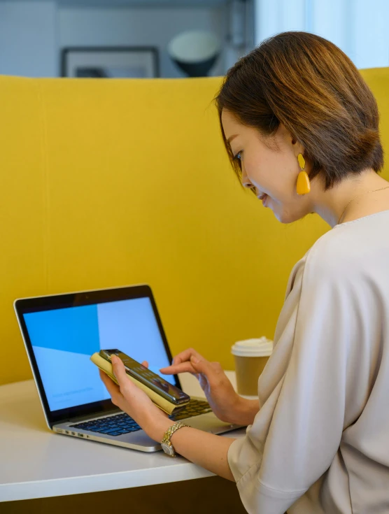 a woman holding a cell phone and looking at her laptop