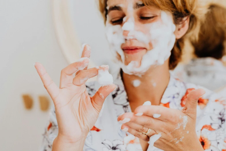 a woman in white flowers shirt using cream on her face