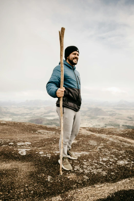 a man holding an old wooden stick on top of a hill