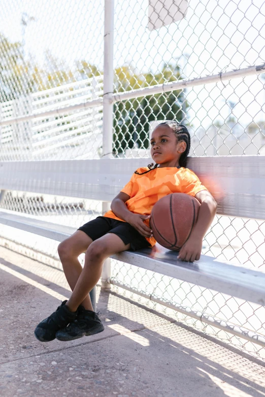 an african american boy sits on a bench while holding a basketball