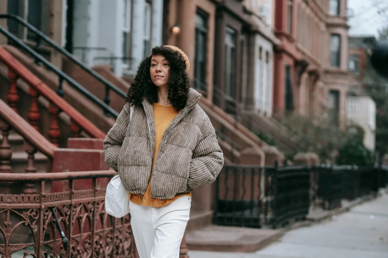 a woman wearing white pants and a grey jacket walking down the street