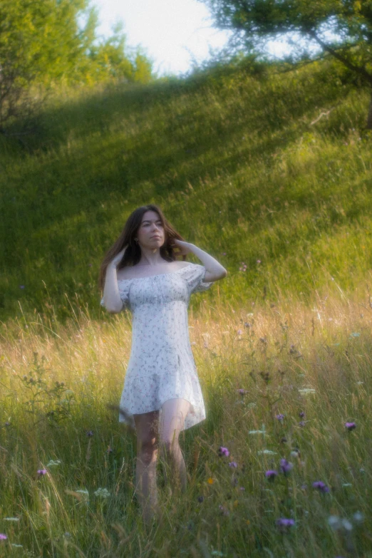 a woman in a dress standing in a field with trees in the background