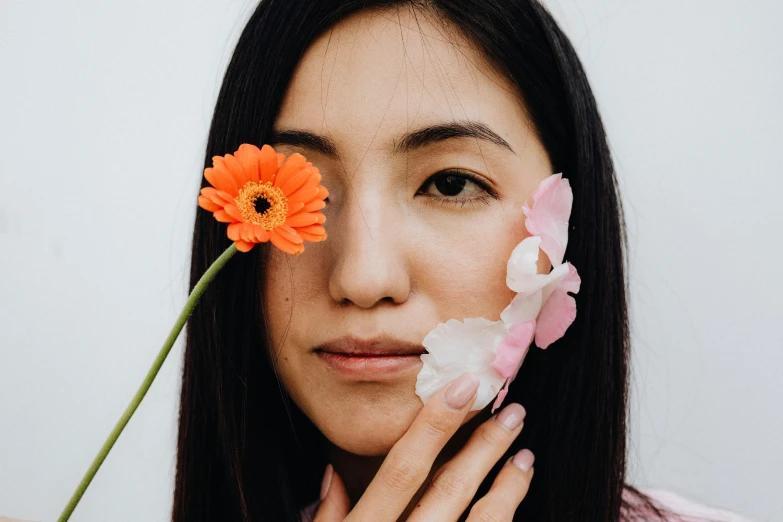 a woman holding up a flower with her hand to her face