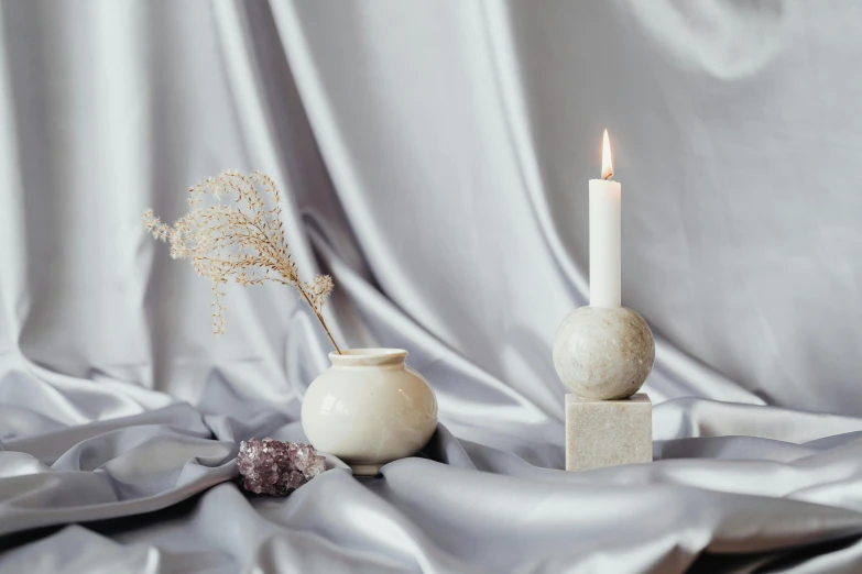 a white candle sits on a blanket next to two small vases