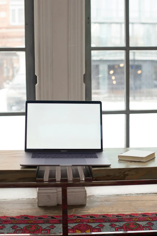 a white laptop computer sitting on a desk by a window