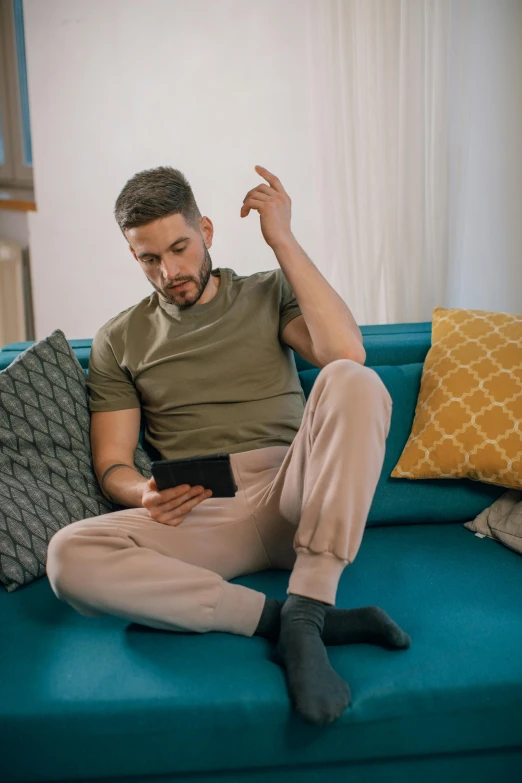 a young man sitting on a couch looking at a tablet
