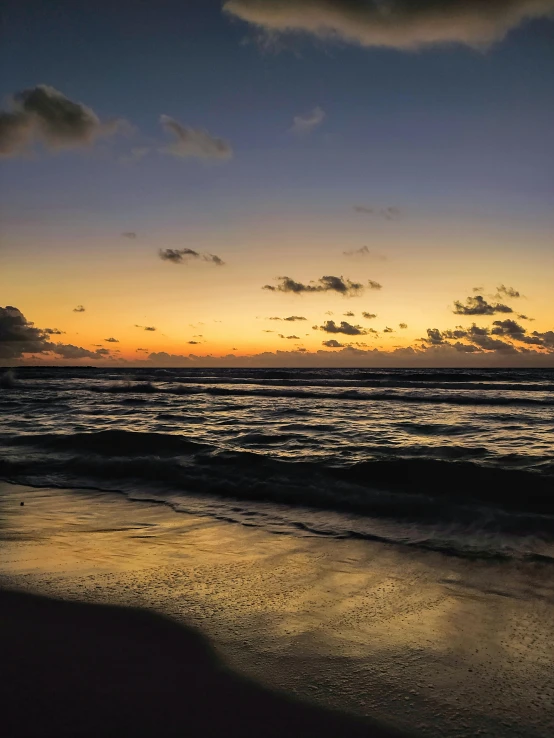 a couple of people walking along a beach with the ocean and clouds above