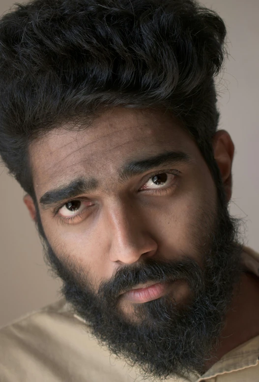 a young man with a beard, mustache and moustache looks at the camera