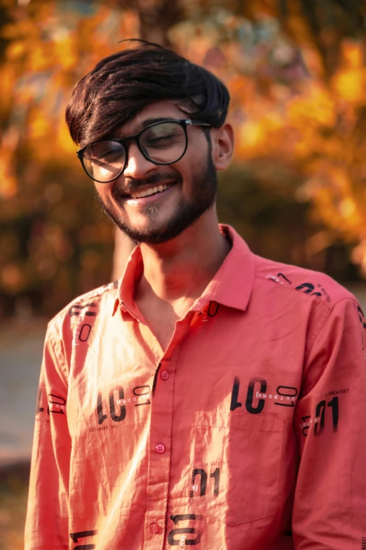 a man with long hair, glasses and orange shirt smiles