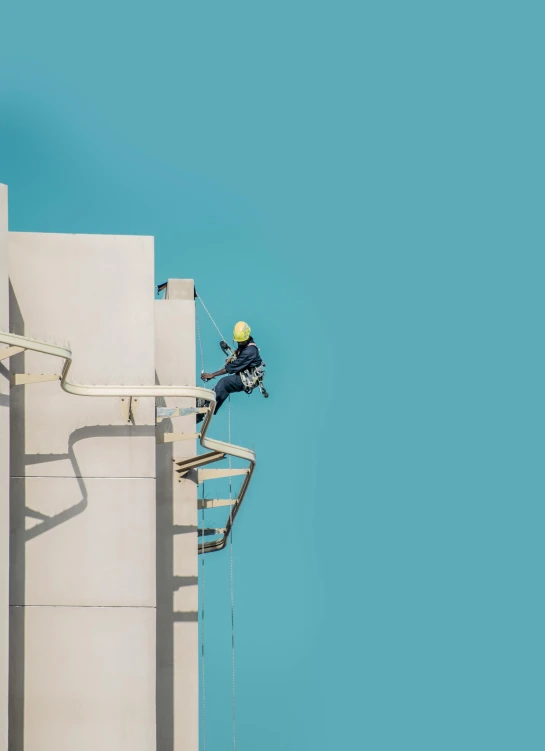 a man with a safety helmet and jacket is hanging on to the wall