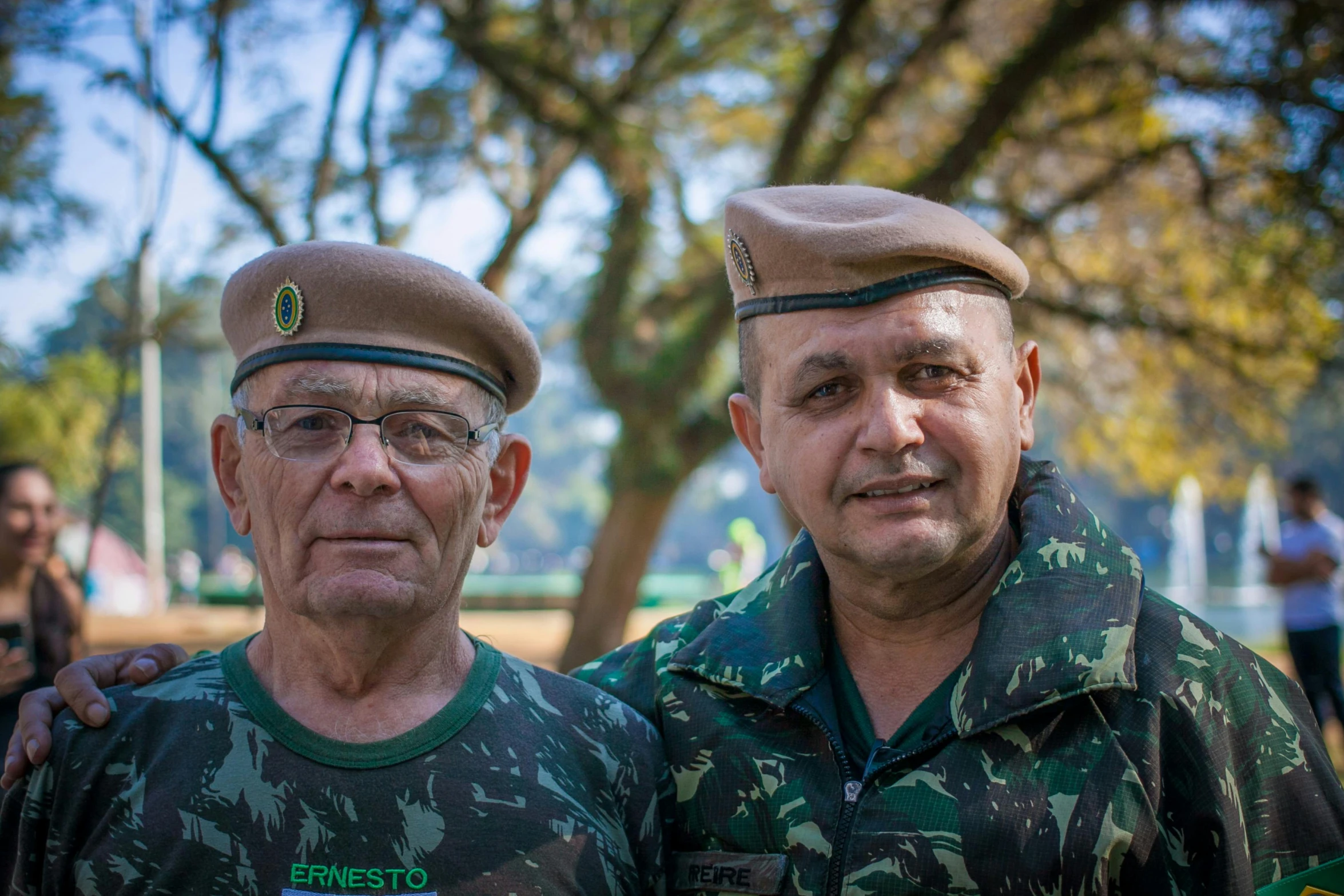 two men wearing military uniforms standing in front of trees