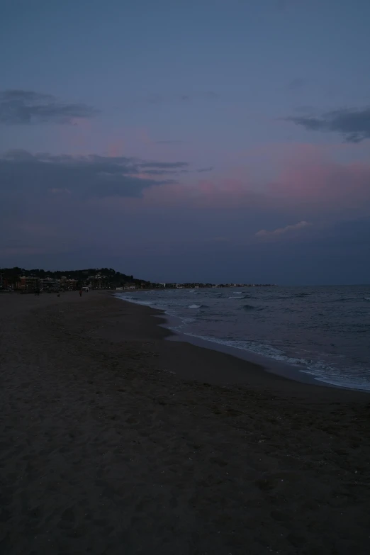 a dark sky at night with the sun rising and people walking along the beach