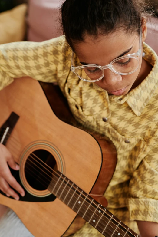 girl wearing glasses plays guitar on couch