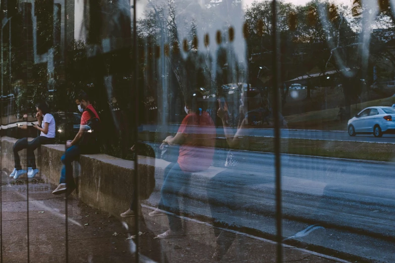 four people sit on the curb while others are walking along