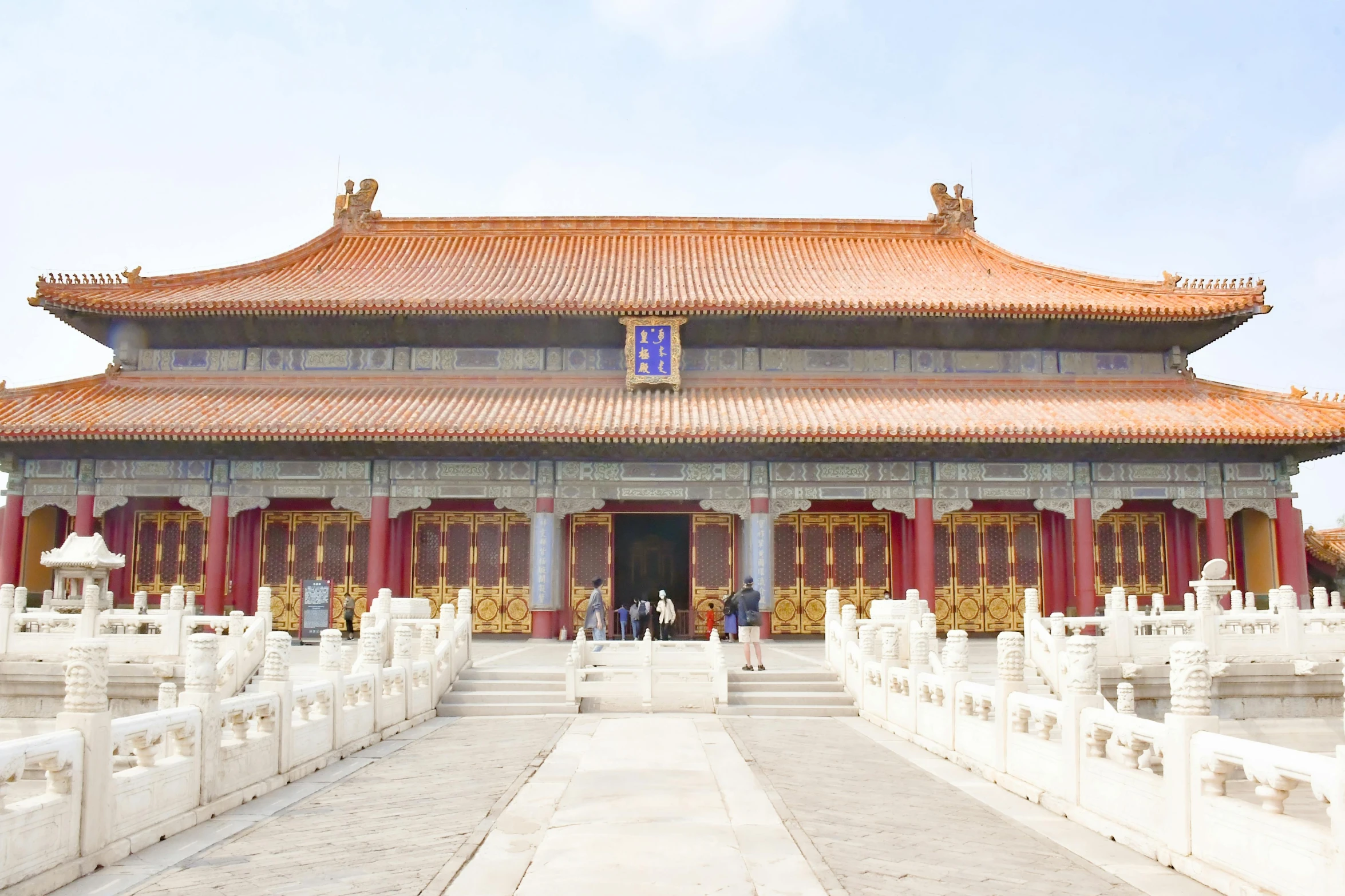 people walk towards a white building with red and yellow accents