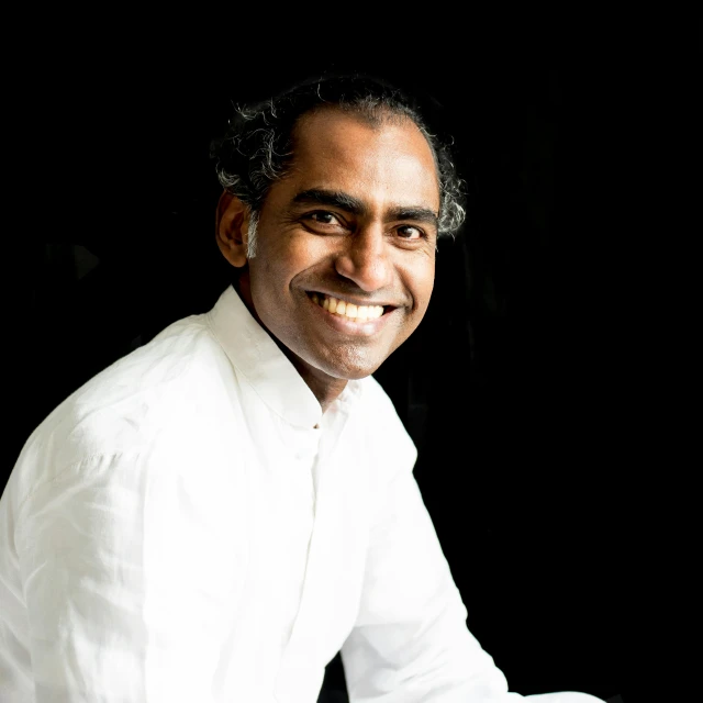 a man wearing white is smiling while sitting on the floor