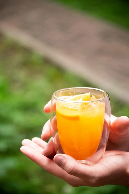 a person holding out a glass with juice in it